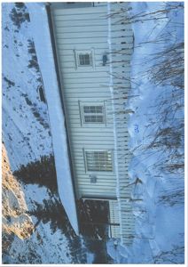 Fotografi av en hvit bygning med horisontale panelvegger og vinduer, sett fra siden i et snødekt landskap.