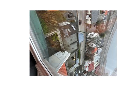 Fotografi tatt fra et vindu som viser utsikt over nabolag, gater og tak fra en høyde.