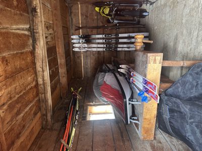Fotografi av en innendørs skogsskuff eller skur med skøyter, ski og utstyr hengende på vegger og gulv.