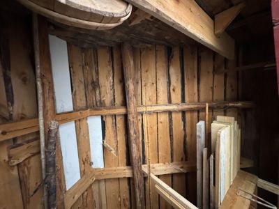 Fotografi av en gammel, rustikk trekonstruksjon, sannsynligvis et takrom eller loft med synlige bjelker og paneling.