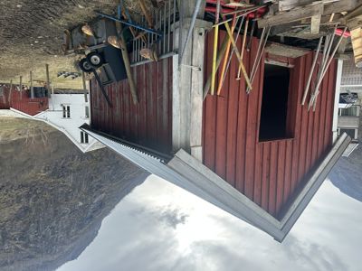 Fotografi av en rød bygning under ombygging eller vedlikehold, med synlig takkonstruksjon og verktøy.