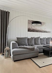 Fotografi av et innredet stueområde med en grå sofa, en bueformet gulvlampe og hvite panelvegger.