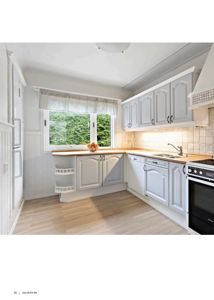 Fotografi av en kjøkkeninnredning med hvite skap, trebenk og lys gulv.