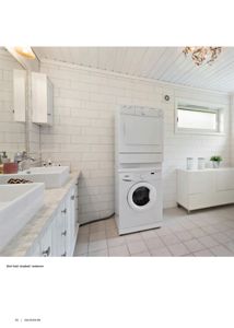 Fotografi av et innredet bad/vaskerom med hvite fliser, vask, vaskemaskin og tørketrommel.