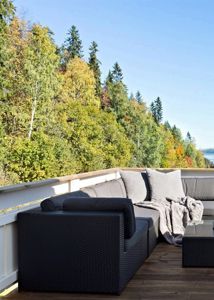 Fotografi av en terrasse med utemøbler og utsikt over skog og vann.