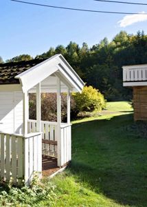 Fotografi av en hvit veranda eller paviljong på en grønn tomt med skog i bakgrunnen.