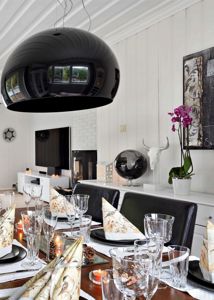 Fotografi av et innredet spisestue- og stueområde med en stor svart hengelampe, et spisebord og en TV.