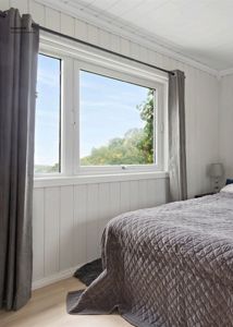 Fotografi av et innredet soverom med en stor vindu, gardiner og en seng.