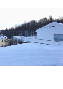 Fotografi av en hvit bygning med snø på taket og i forgrunnen, sett fra et lavt vinkel.