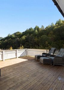 Fotografi av en uteplass med tredekk og hvit hekk, med utsikt over skog.
