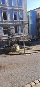 Fotografi av en gatemiljø med en bygning i bakgrunnen, en kunstnerisk skulptur i forgrunnen og en trafikkplate.