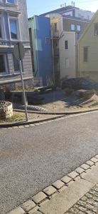 Fotografi av en gatekryssing med flere bygninger i bakgrunnen, en bil og et trafikktegn.