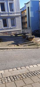 Fotografi av en gatenevning med fasader på nabohus, en bil og en plantepott.