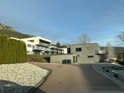 Fotografi av en moderne bygning med flere etasjer, sett fra en vei med en bakgrunn av fjell og trær.