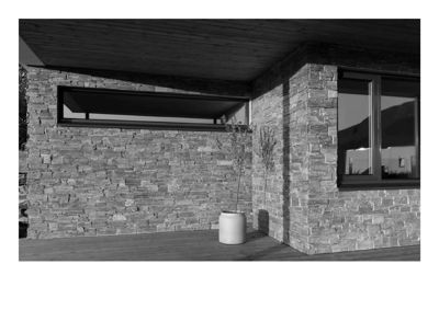 Fotografi av en fasade på en bygning med steinmur, vinduer og en uteplass.