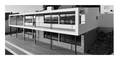 Sort-hvitt fotografi av en moderne, toetasje bolig sett fra siden. Bygningen har store glassflater, en utvendig trapp og en moderne fasade.