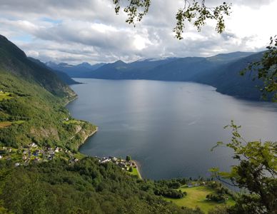 Fotografi av et landskap med fjord, fjell og hus langs kysten.