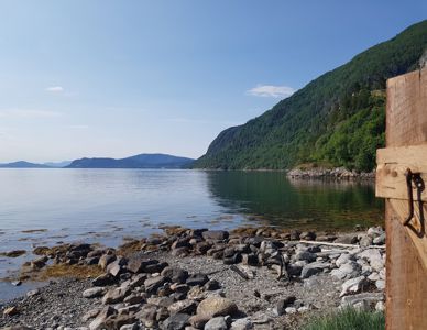 Fotografi av en kystlinje med fjell, vann og en steinstrand.