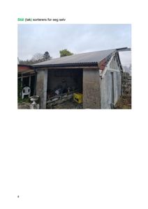 Fotografi av en eksisterende bygning (en utedekkning eller garasje) med betongvegger og et stålplate-tak.