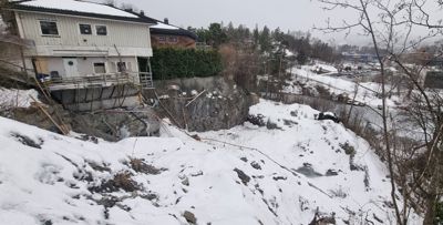Fotografi av en boligbygning på en bratt, snødekt skråning med en steil klippvegg under huset.
