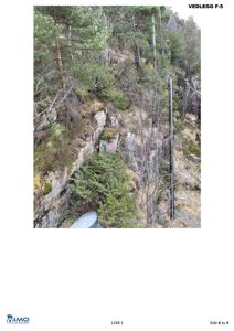 Fotografi av et steinete, skogkledt terreng med en metallstolpe eller kabel i forgrunnen.