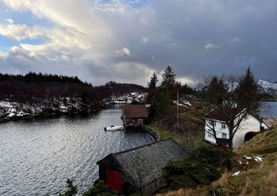 Fotografi av en bygning ved vannet med omgivende natur.