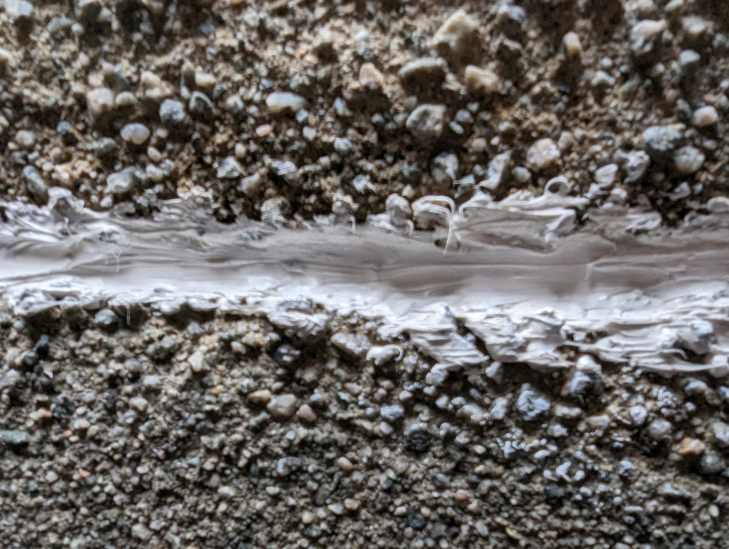 Et nærbilde (makrofoto) av en sprekke i en betongflate, fylt med hvit fugefylling eller lim.