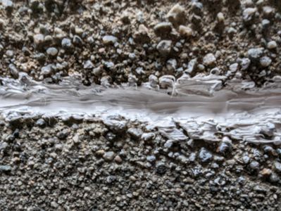 Et nærbilde (makrofoto) av en sprekke i en betongflate, fylt med hvit fugefylling eller lim.