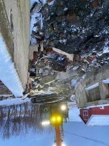 Fotografi av en byggeplass eller riveplass med en graver som jobber, snø og ruiner.