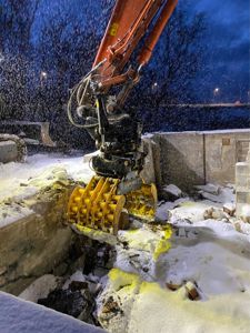 Fotografi av en gulett som bryter ned en betongfundament under snøfall.