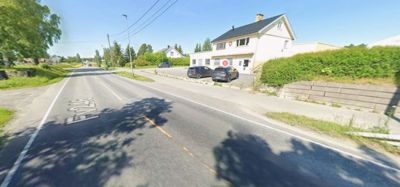 Fotografi av en vei (Fv26) med en hvit villa og en mindre bygning på høyre side.