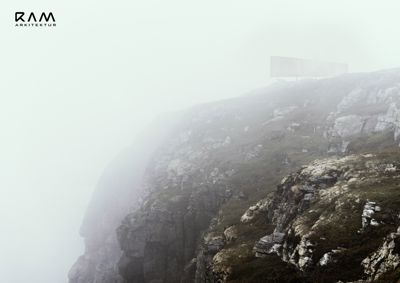 Fotografi av en kystklipp med tåke og et fjerntliggende, uklar objekt på toppen.