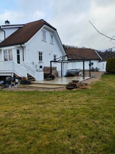 Fotografi av en hvit villa med tak, terrasse og utemøbler sett fra bakgården.