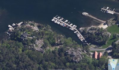 Flyfoto eller satellittbilde av et kystområde med båthavner, hus og natur.