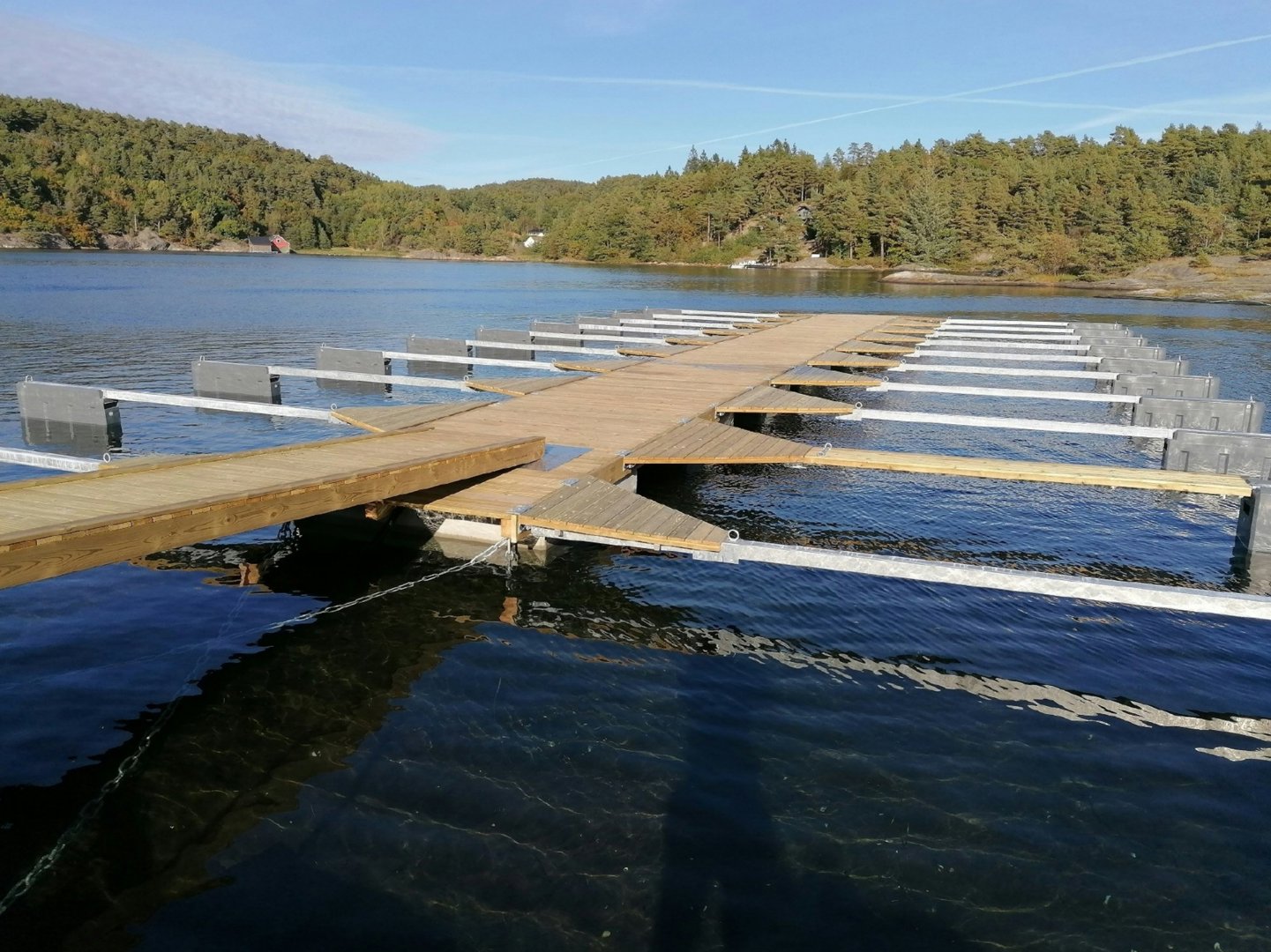 Fotografi av en kai eller brygge som strekker seg ut i vannet, med skogkledde kystlinjer i bakgrunnen.