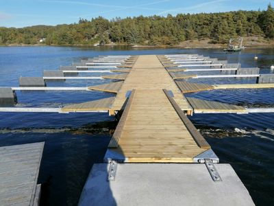 Fotografi av en nybygd kai med utstikkende båtplatser, sett fra land mot vannet.
