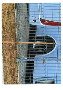 Fotografi av en bil sett gjennom et gjerne, med grus og gress i bakgrunnen.