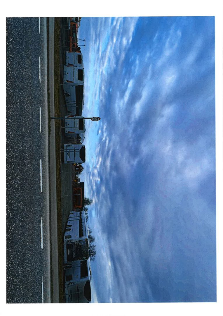 Fotografi av en vei med flere busser parkert langs siden, sett mot en skyet himmel.