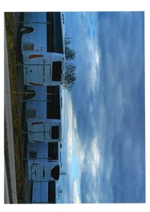 Fotografi av en hvit busk eller buss sett fra siden, med en skyet himmel i bakgrunnen.