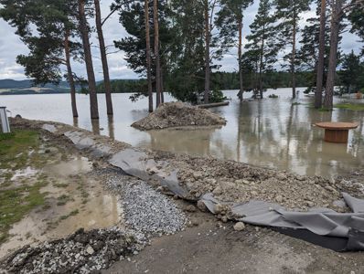 Fotografi av et utsnitt fra en byggeplass ved vannet, som viser graving, materialer og delvis oversvømmelse.