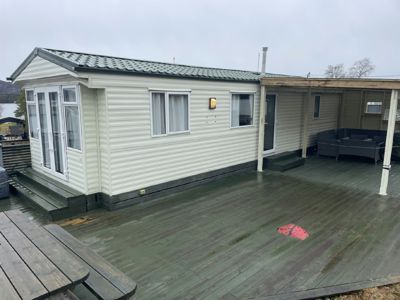 Fotografi av en ferdigbygd hytte eller mobilheim sett fra siden, med en stor terrasse foran.