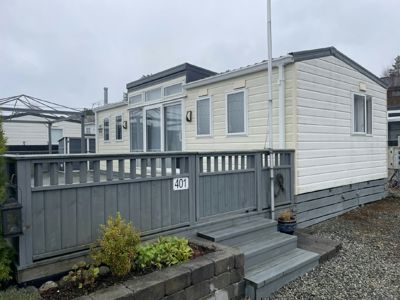 Fotografi av en hvit mobilheim eller containerbolig med grå veranda og trapp, sett fra siden.