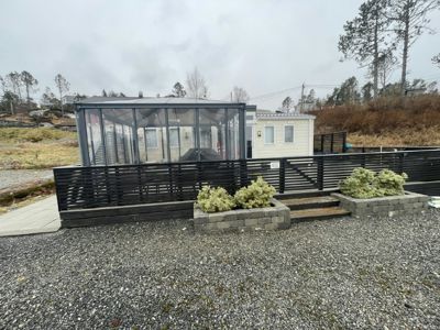 Fotografi av en ferdig eller nesten ferdig bygning med en moderne glassfasade, en mørk hekk og en grusbeplantet hage.