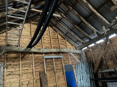 Fotografi av en eksisterende, rustikk bygning med synlig tømmerkonstruksjon, tak og innvendige detaljer.