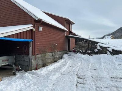 Fotografi av en rød, trepanelt bygning (garasje eller uthus) med snø på taket og i omgivelsene.