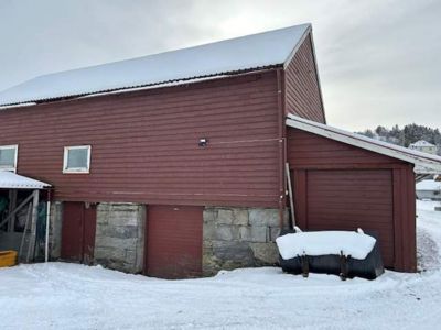 Fotografi av en rød, langbygget skur eller uthus med steinfundament, sett fra siden. Bygningen har snø på taket og i omgivelsene.