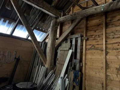 Fotografi av en utelagret eller uferdig bygning med synlig tømmerkonstruksjon, tak og lagrede materialer.