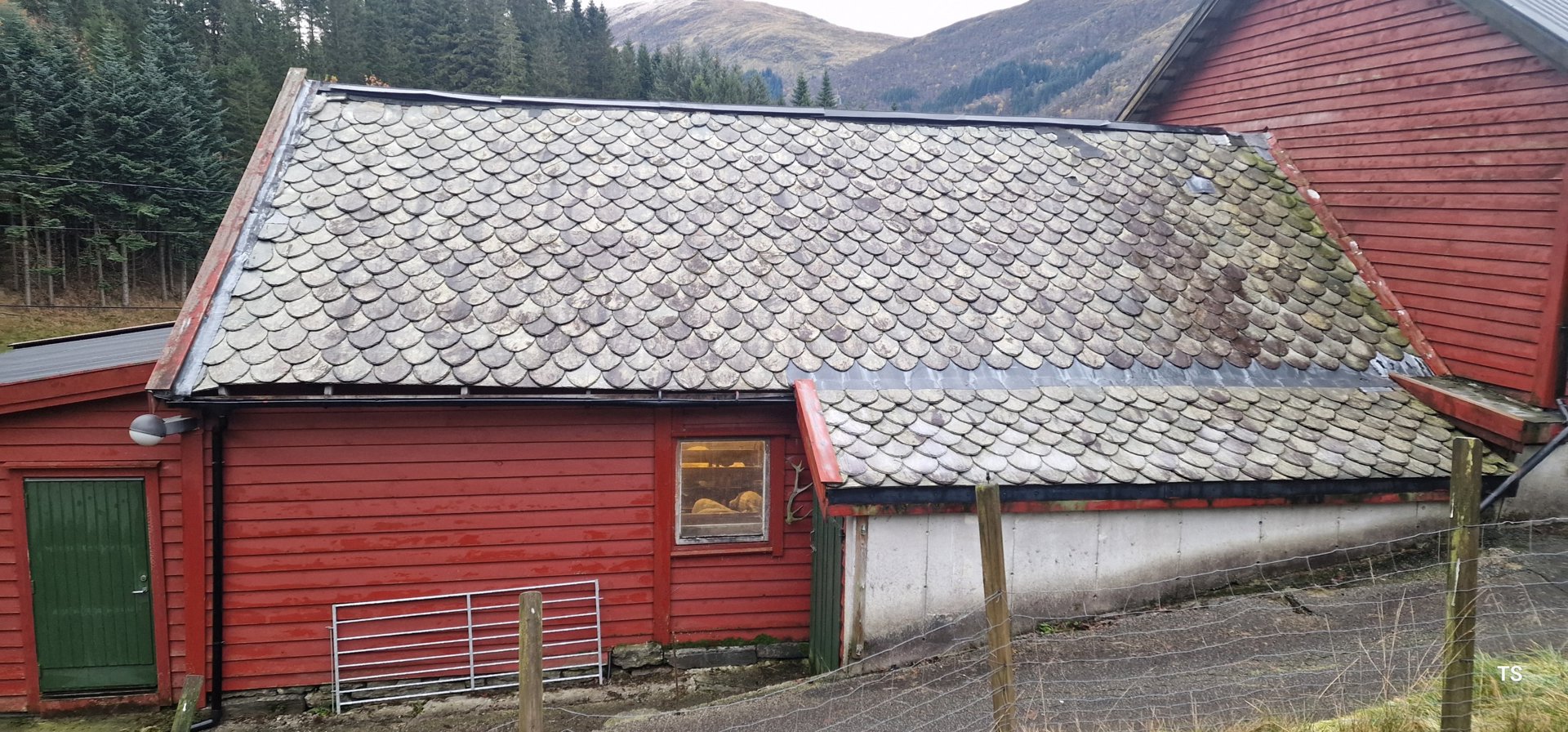 Fotografi av en rød bygning med tak av skiferplater, sett fra siden.