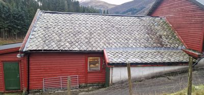 Fotografi av en rød bygning med tak av skiferplater, sett fra siden.