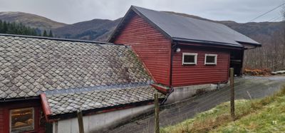 Fotografi av en rød bygning med skifer- og blikkdekke, sett fra siden med fjell i bakgrunnen.